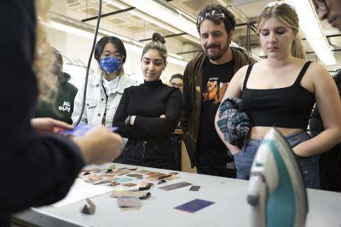 Jewellery Community Group of AUArts students and an instructor gathered around a table observing samples of textured and colored metal pieces.