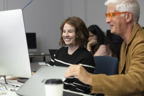 AUArts student and faculty member smiling while working together at a computer in class.