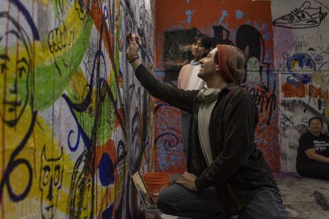 Student painting colorful graffiti art on a wall while others watch in the AUArts graffiti stairwell.