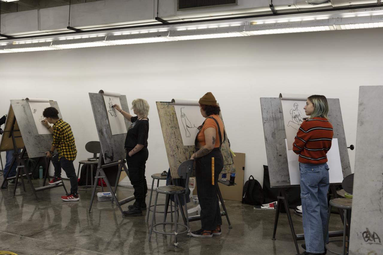 Students stand at easels sketching figure drawings in an AUArts classroom.