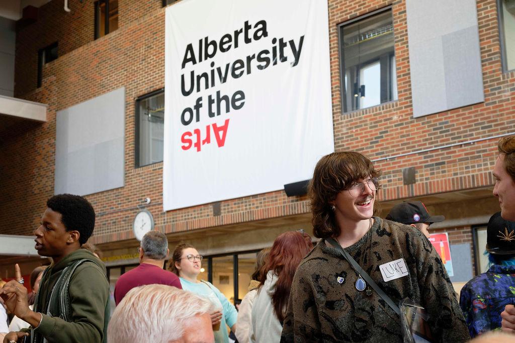Students gather in AUArts’ main hall during orientation, chatting under a large Alberta University of the Arts banner.
