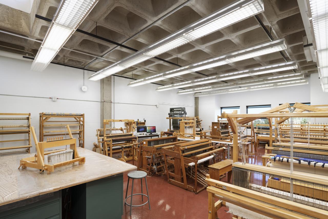 Fibre Studio AUArts fibre studio with rows of wooden floor looms and weaving equipment in a bright, spacious classroom.