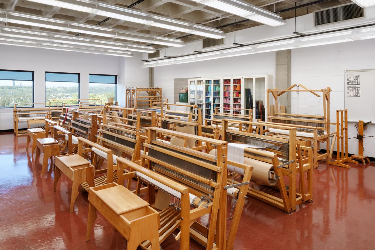 Loom Room AUArts loom room with rows of wooden floor looms, stools, and shelves of colourful yarn.