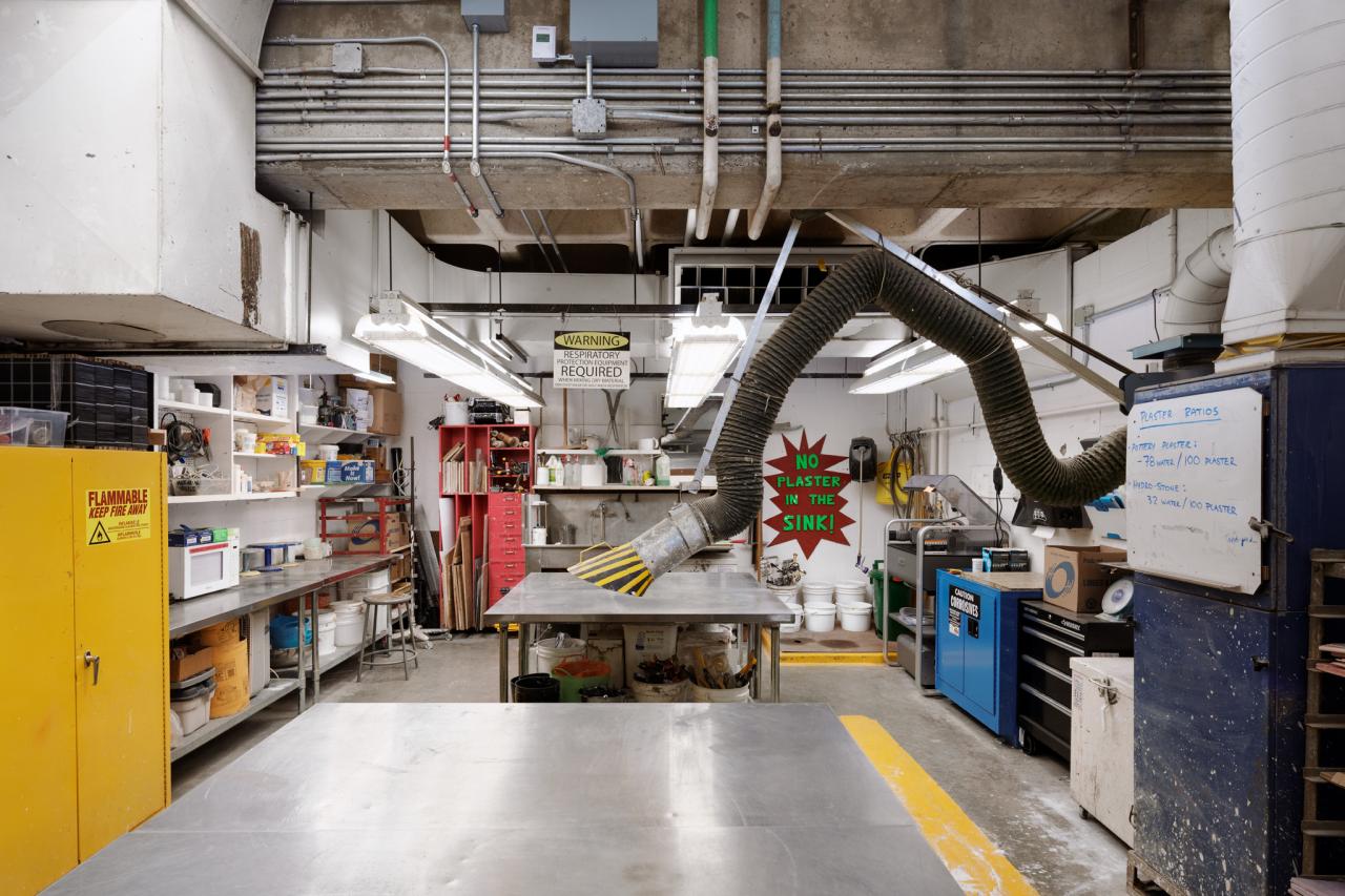Metal Shop 2 AUArts metal shop work area with large ventilation hose, stainless steel worktables, and shelves stocked with tools and supplies.