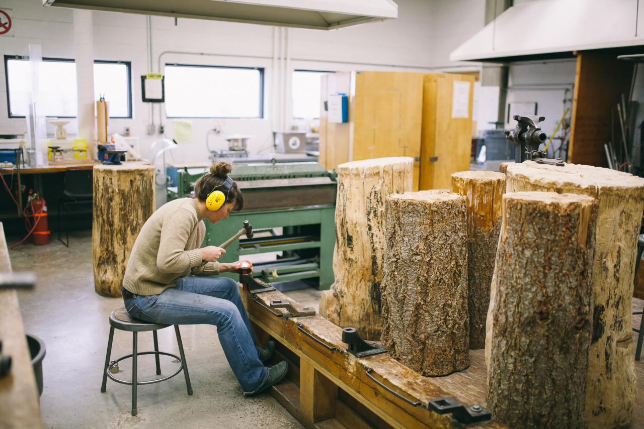 Jewellery Studio Student wearing ear protection hammering metal on a stump in the AUArts jewelry and metals studio.