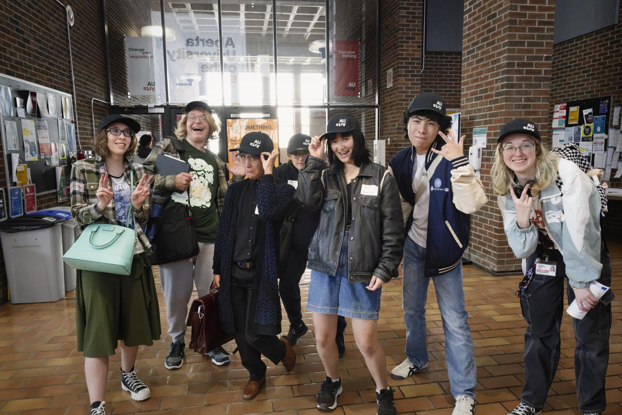 Open House Banner A group of smiling AUArts students pose together in the campus main mall, wearing matching black AUArts caps and making playful hand gestures during Orientation Day.