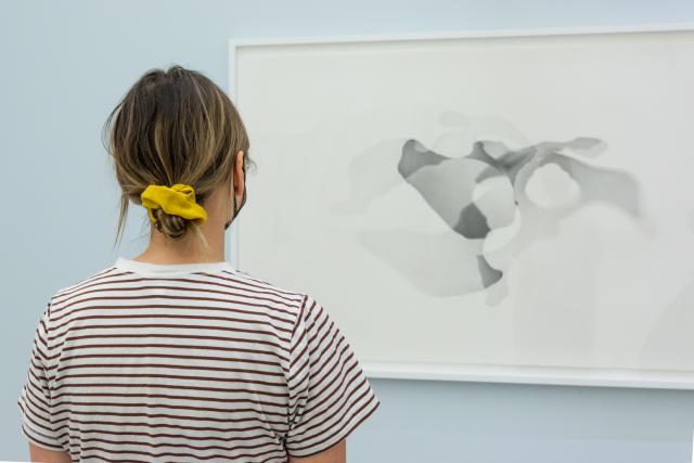 viewer looks at framed graphite drawings in a gallery