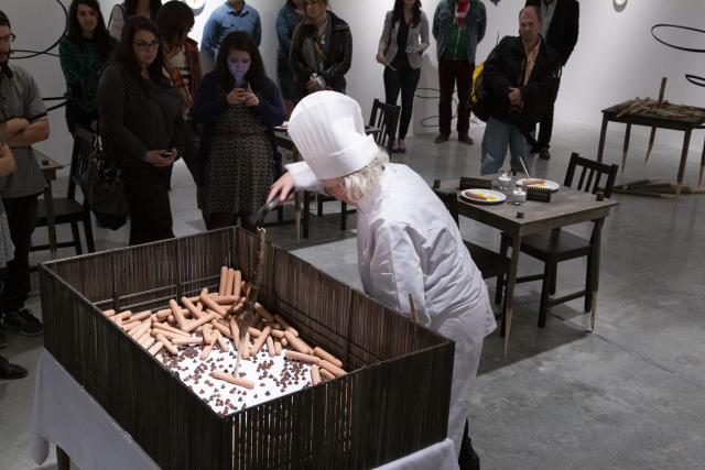 Finally the artist is in the gallery dropping the wild hot dogs into a wooden cage.