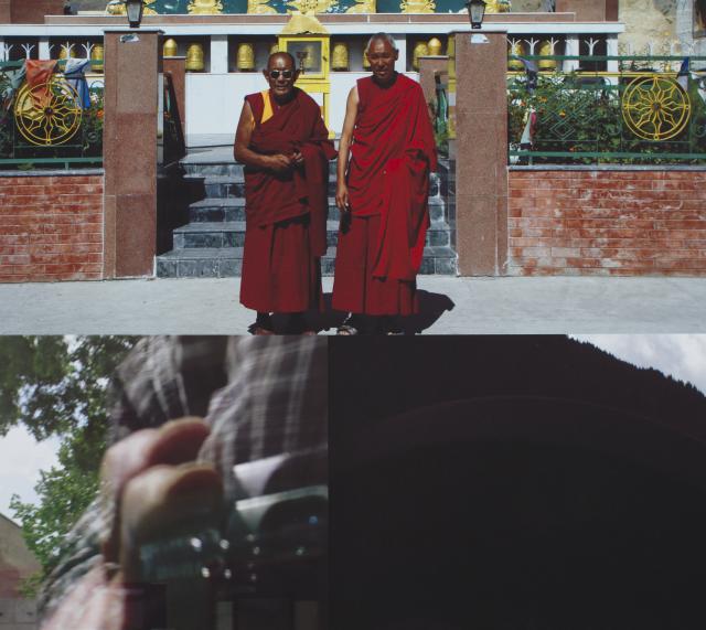Detail of one of the prints. There are two monks standing outside a building. Underneath the is a blurred image of someone holding a camcorder.