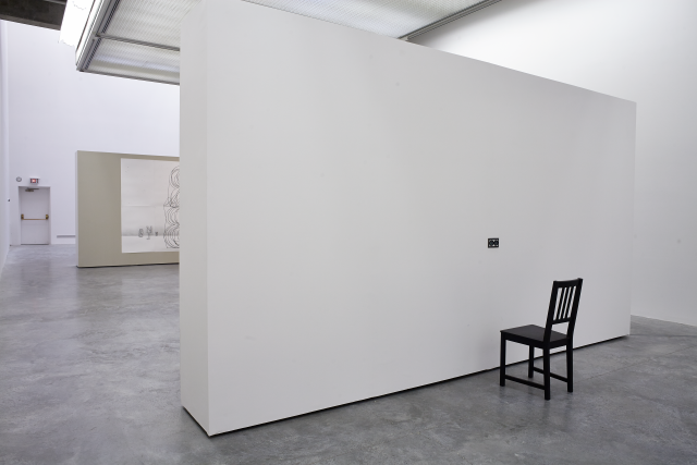 Wide view of the gallery. We see the large scale architectural sketch and a chair with a peephole of sorts at eye level. 