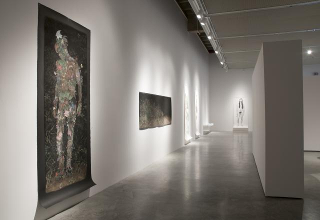 Wide shot of the gallery. Looking down a corridor we can see some of the hung pastel drawings. There are five visible. 