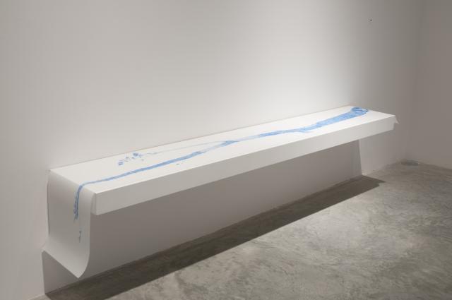 Detail of Stick-Man (2011). The long drawing is draped over a low shelf. The blue pencil image depicts a long stick with some flora. 