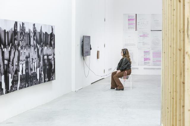 Person sitting on a stool with headphones to watch a video installation from The Beyond Within