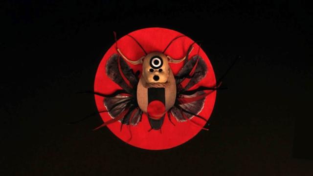 A striking surreal composition featuring a beetle-like creature with a central eye motif against a bold red circle, blending sculpture and symbolism in an imaginative frame.