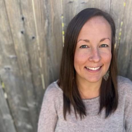 continuing education instructor Amy Bouchard standing against a brown wooden fence wearing grey sweater