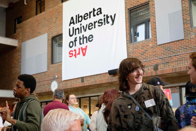 Why choose AUArts? Students gather in AUArts’ main hall during orientation, chatting under a large Alberta University of the Arts banner.