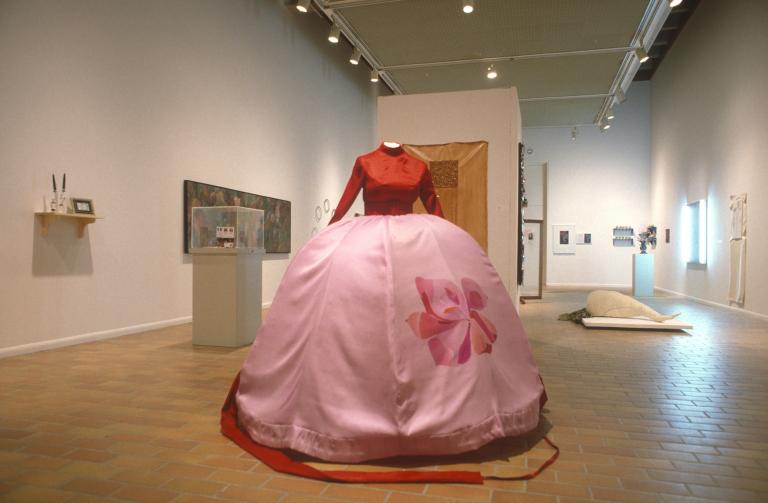 Jenifer Darbellay's textile work, a ballgown with a huge domed skirt displayed on a dress mannequin, in the 1996 ACA Grad Show in the Illingworth Kerr Gallery. The gown has a deep red long-sleeved bodice and the huge pink skirt has a red floral image printed on one panel of the fabric