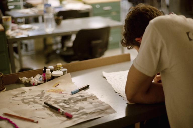 Student sketching at a studio desk with drawing materials in an Alberta University of the Arts creative workspace.