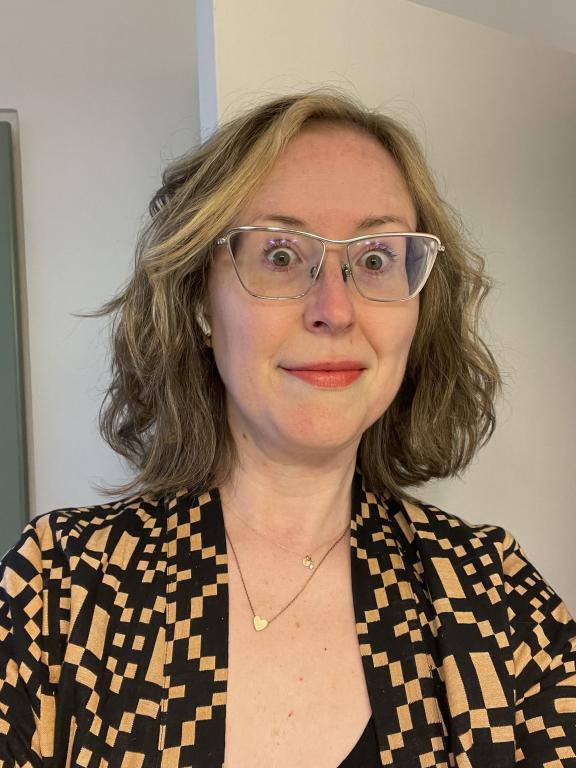 Portrait of mixed-media artist Heather Huston wearing glasses and a black-and-gold patterned jacket.